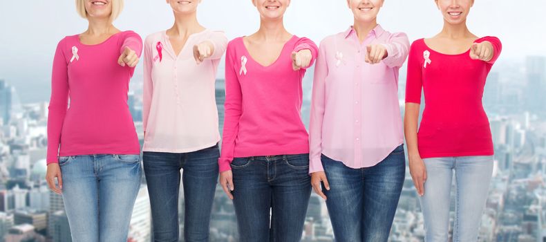 healthcare, people, gesture and medicine concept - close up of smiling women in blank shirts with pink breast cancer awareness ribbons pointing on you over city background