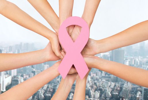 healthcare, people and medicine concept - close up of women hands with paper cancer awareness symbol over city background