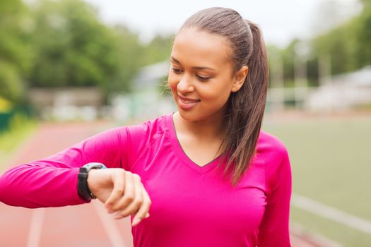 fitness, sport, training, technology and lifestyle concept - smiling african american woman with heart-rate watch on track outdoors