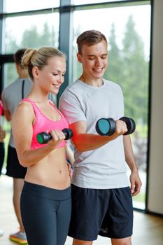 fitness, sport, exercising and diet concept - smiling young woman and personal trainer with dumbbells in gym