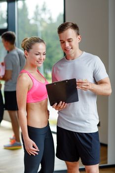 fitness, sport, exercising and diet concept - smiling young woman with personal trainer in gym