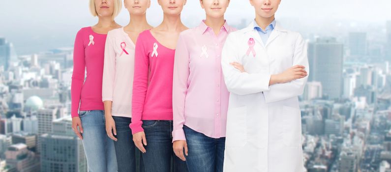 healthcare, people and medicine concept - close up of women in blank shirts with pink breast cancer awareness ribbons over city background