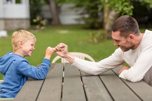 family, happiness, generation, home and people concept - happy father and son doing arm wrestling outdoors