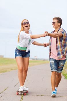 holidays, vacation, love and friendship concept - smiling couple with skateboard riding and holding hands outdoors