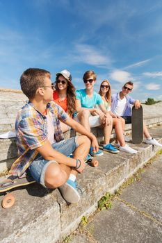 friendship, leisure, summer and people concept - group of smiling friends with skateboards sitting on city street