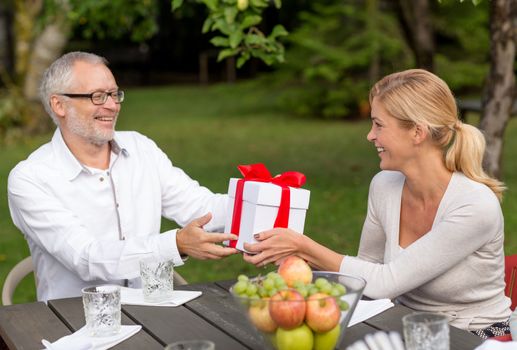 family, happiness, generation, home and people concept - happy family with gift box having holiday dinner outdoors