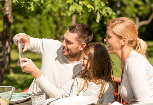 family, happiness, generation, home and people concept - happy family sitting at table and taking selfie with tablet pc computer outdoors