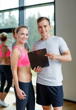 fitness, sport, exercising and diet concept - smiling young woman with personal trainer in gym