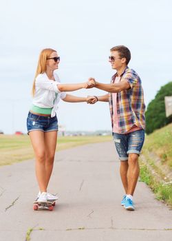 holidays, vacation, love and friendship concept - smiling couple with skateboard riding and holding hands outdoors