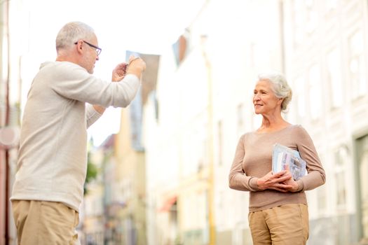 age, tourism, travel, technology and people concept - senior couple with map and camera photographing on street