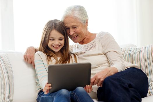 family, generation, technology and people concept - smiling granddaughter and grandmother with tablet pc computer sitting on couch at home