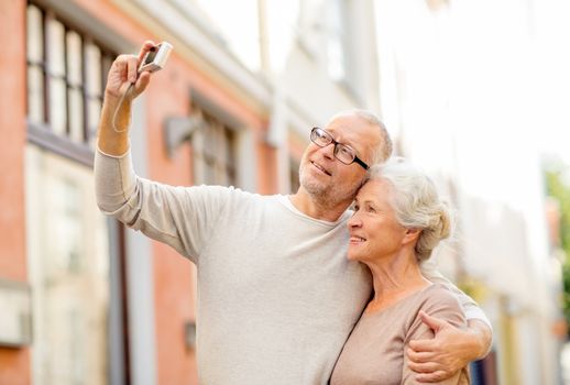 age, tourism, travel, technology and people concept - senior couple with camera taking selfie on street