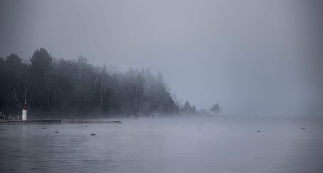 Heavy blanket of fog lifting off the Ottawa River revealing a small peninsular forest and lighthouse, Ontario Canada.