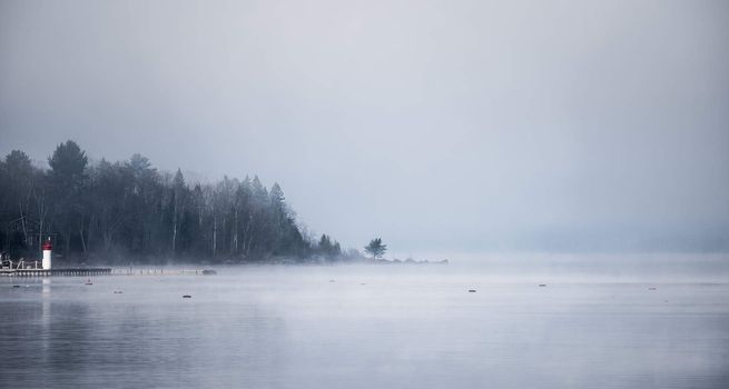 Heavy blanket of fog lifting off the Ottawa River revealing a small peninsular forest and lighthouse, Ontario Canada.