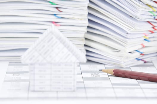 Brown pencil on finance account have blur house as foreground and pile of paperwork as background.