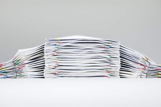 Colorful paper clip with pile of report on white table.