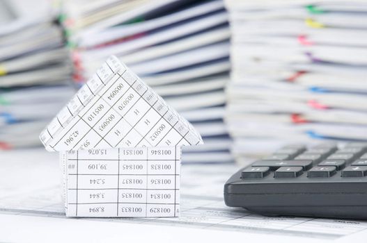 House and calculator on finance account have blur pile of paperwork as background.