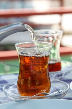 Close up detailed view of teapot pouring hot black tea into the glass.