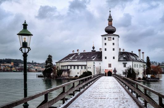Snow covered wooden bridge leading to a white church on a lake island in Gmunden near Salzburg, Austria