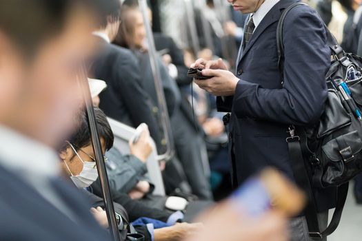 Interior of moder Tokyo metro with passengers on seats and businessmen using their cell phones. Corporate business people commuting to work by public transport. Horizontal composition.