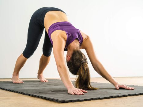 Photo of a healthy young woman doing the downward dog yoga position on a black floor mat.