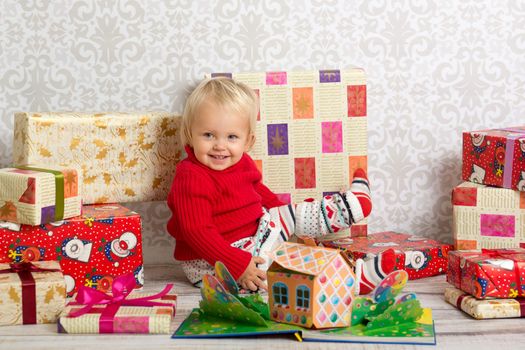Dressed festively girl with stacks of present boxes around sitting on the floor and smiling.