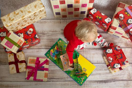 Dressed festively girl with stacks of present boxes around sitting on the floor and playing with paper gingerbread house.