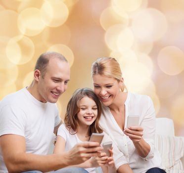 family, holidays, technology and people concept - smiling mother, father and little girl with smartphones over beige lights background