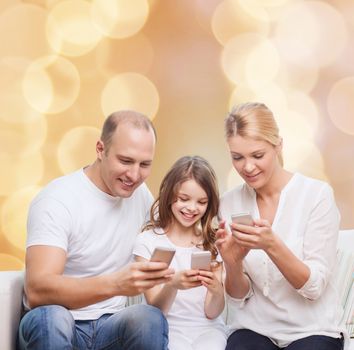 family, holidays, technology and people concept - smiling mother, father and little girl with smartphones over beige lights background