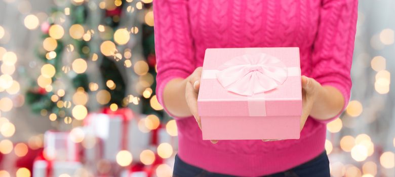 christmas, holidays and people concept - close up of woman in pink sweater holding gift box over tree lights background