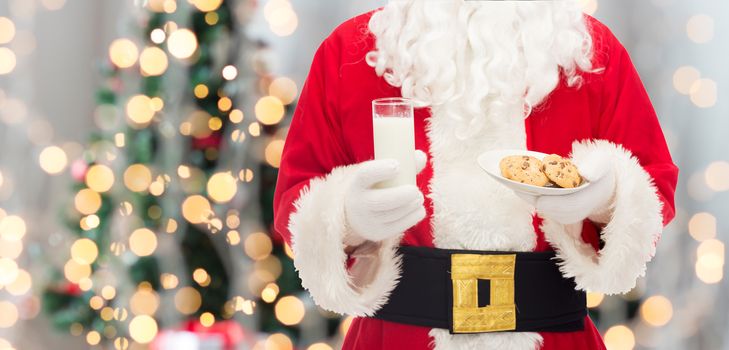 christmas, holidays, food, drink and people concept - close up of santa claus with glass of milk and cookies over tree lights background