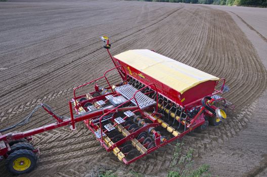 Tractor sowing crop wheat seeds in freshly plowed farm field 