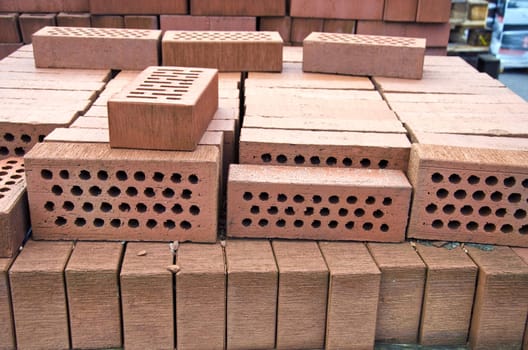 Stack of red clay bricks with holes in market