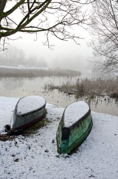 One green and one blue upturned boat in winter by the lake 