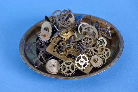 Metal plate full of brass clock gears on blue background