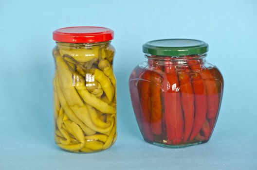 Vegetables peppers preserved in two glass jars on blue backgroun