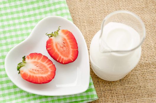 Strawberries and milk drink in glass on tablecloth and sack background.