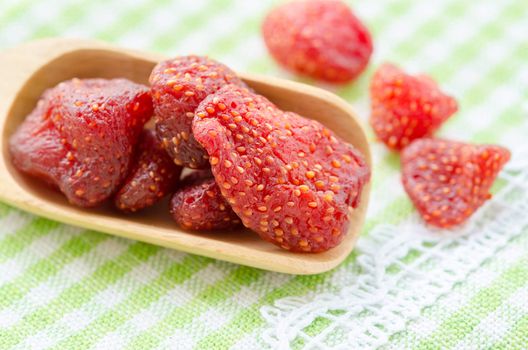 Dried strawberries in wooden spoon on tablecloth.