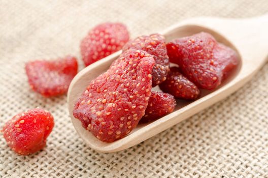 Dried strawberries in wooden spoon on sack background.