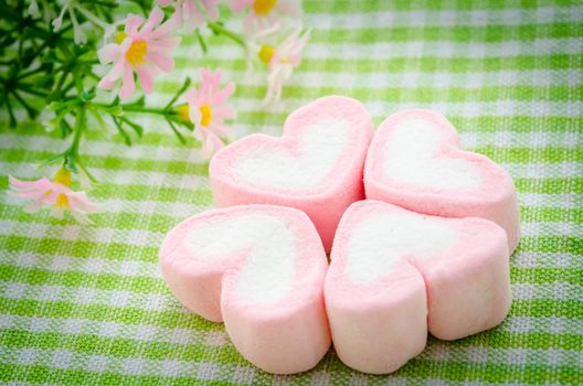 Pink marshmallow heart shape with flower on table cloth.