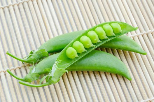 Fresh green peas pods on bamboo mat background.