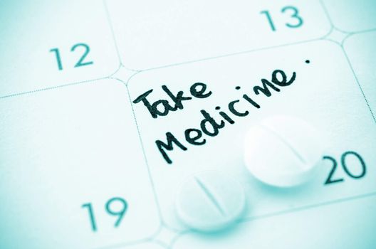 Reminder take medicine written and Medicine pills on calendar.