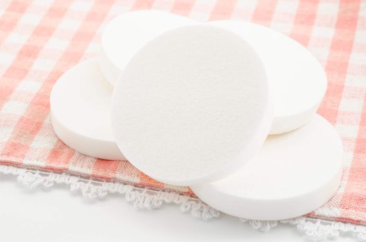 White cosmetic circle sponges for makeup on tablecloth.