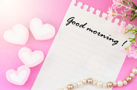 Good morning written with sweet heart shape of pink marshmallows with flower on pink background.