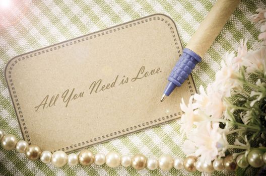 All you need is love message writing on brown paper tag with pen and flower on cloth background.