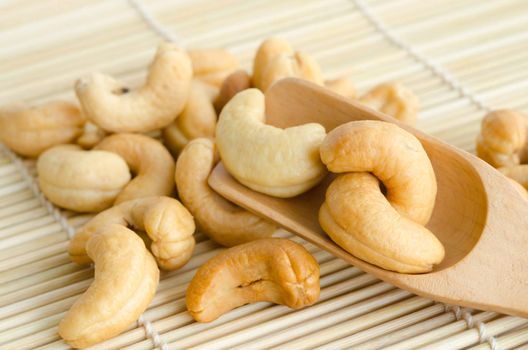 Heap of a roasted cashew nuts in wooden spoon on wood background.