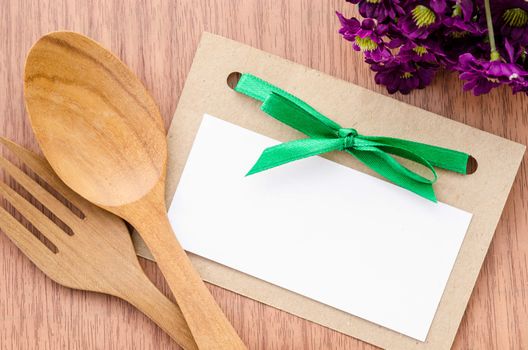 Blank paper tag and wooden spoon with flower on wooden background.