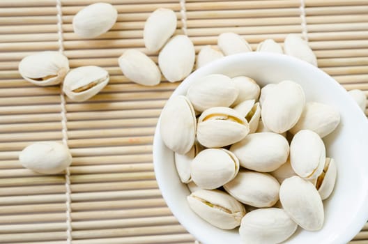 Pistachio in white cup on bamboo mat on white background.