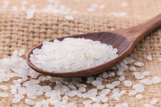 Whole grain traditional japanese rice  in wooden spoon with hemp sacks background