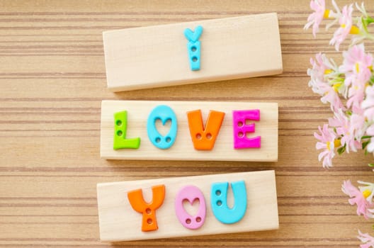 Colorful alphabet of LOVE wording with flower on wooden background.
